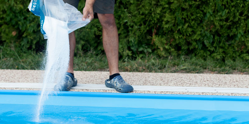 Una persona echando sal en el agua de una piscina con clorador salino